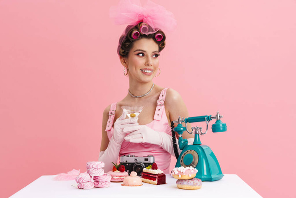 Young woman barbie in pink dress calling on landline phone while sitting at the table over isolated background - Photo, Image