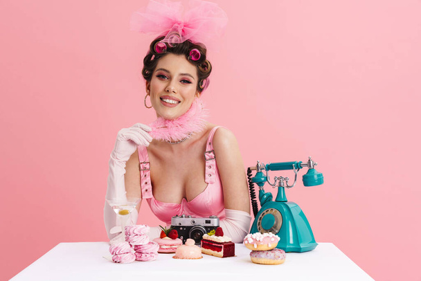 Young woman barbie in pink dress calling on landline phone while sitting at the table over isolated background - Fotografie, Obrázek