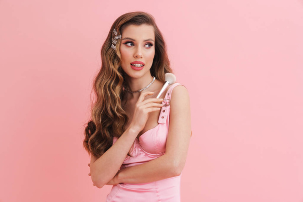 Young white woman wearing dress posing with powder brush isolated over pink background - Foto, immagini