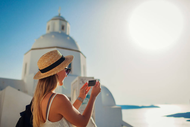 Kobieta turysta robi zdjęcie krajobrazu morskiego na telefon w Fira, Wyspa Santorini spacery przy tradycyjnym białym kościele. Architektura grecka - Zdjęcie, obraz
