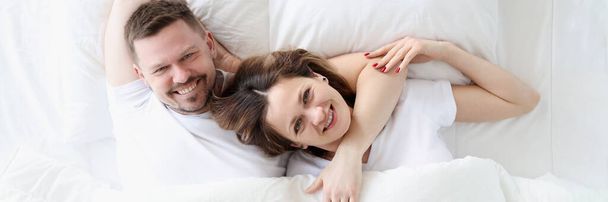 Uśmiechnięty szczęśliwy mężczyzna i kobieta leżą na dużym białym łóżku - Zdjęcie, obraz