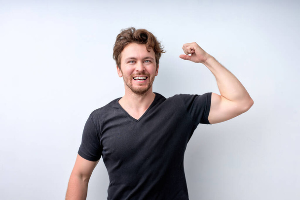 Confident muscular man in casual t-shirt shows muscles on arms, feels proud to be strong - Foto, Bild