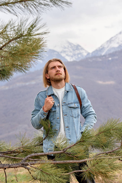 Nice caucasian male in denim jacket stands looking at side in contemplation of mountains - Foto, imagen