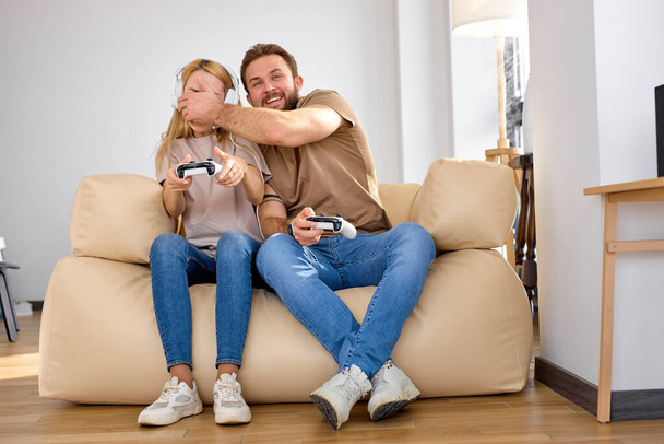 Couple having fun while playing video game at home, holding joysticks in hands - Foto, imagen