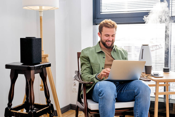 Man work on laptop in room with portable speaker, air purifier, in smart house alone - Φωτογραφία, εικόνα
