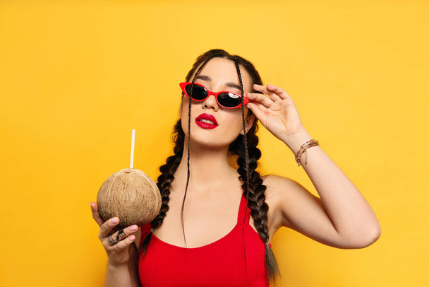 Young woman with fresh coconut on yellow background. Exotic fruit - Zdjęcie, obraz