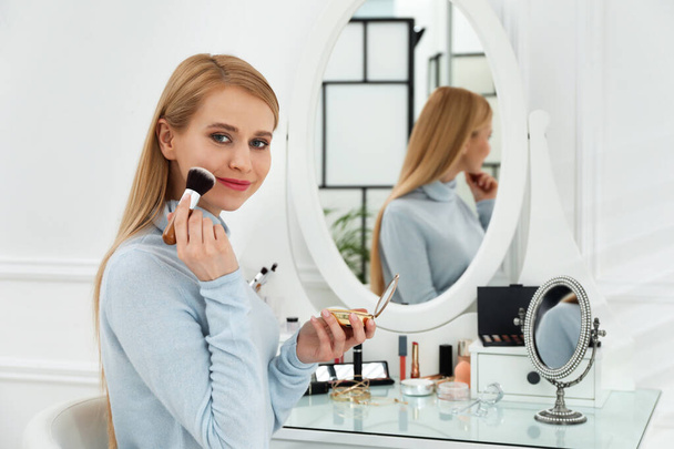 Beautiful woman applying makeup near mirror in room - Photo, Image
