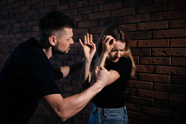 Man abusing scared woman near brick wall. Domestic violence - Foto, afbeelding
