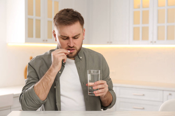 Man taking pill against migraine in kitchen, space for text - Foto, Imagem
