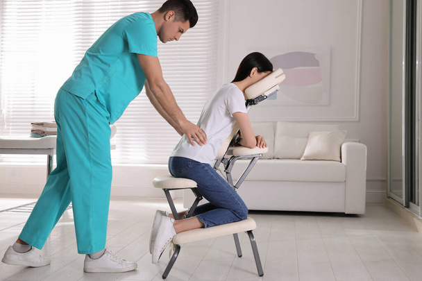 Жінка отримує масаж в сучасному кріслі в приміщенні
 - Фото, зображення