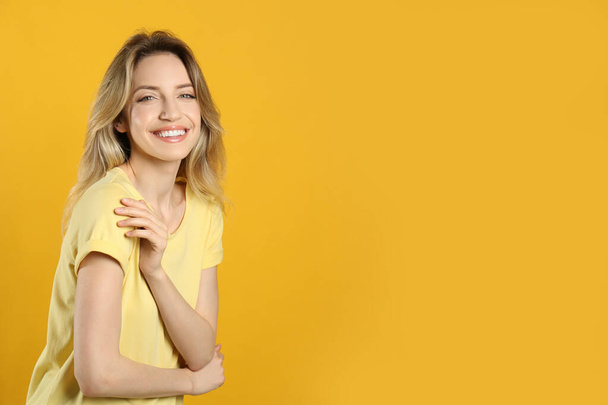 Portrait of happy young woman with beautiful blonde hair and charming smile on yellow background. Space for text - Zdjęcie, obraz