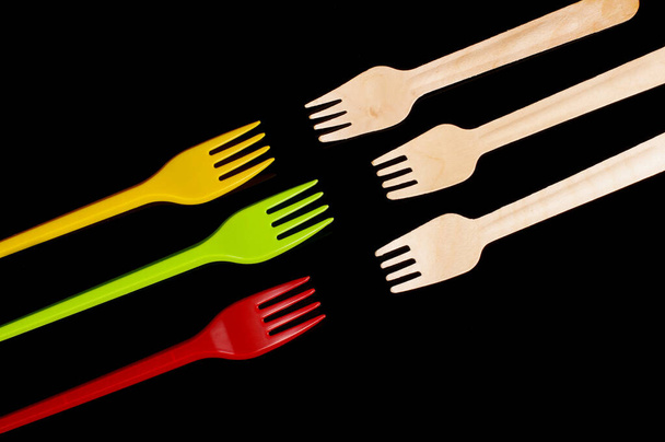 Plastic disposable utensil cutlery forks versus biodegradable wooden disposable utensils isolated on the black background - Photo, Image