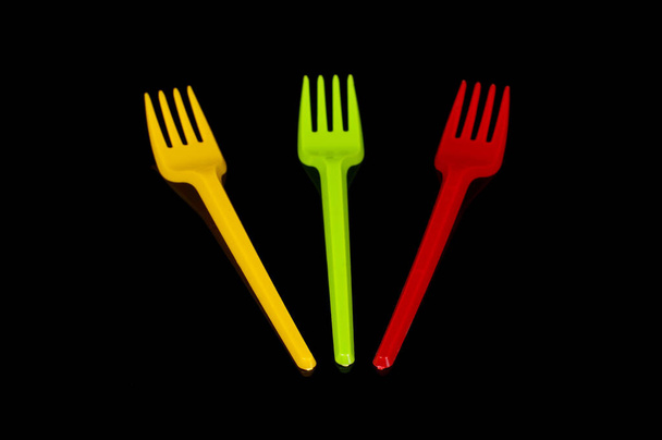 Три пластиковые одноразовые столовые приборы вилки желтый, зеленый и красный (цвета флага Литвы) изолированы на черном фоне - Фото, изображение