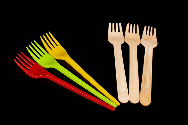 Plastic wegwerpbestek vorken versus biologisch afbreekbaar houten wegwerpgereedschap geïsoleerd op de zwarte achtergrond - Foto, afbeelding