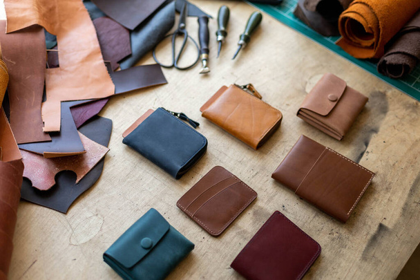 Craftsman hands laying out leatherwork on wooden table at leather workshop. Handwork accessories - 写真・画像