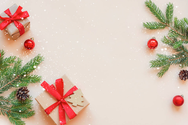 Twee geschenken en groene sparren takken met versieringen op een beige achtergrond. Kerstconcept. Bovenaanzicht, flat lay, kopieerruimte. - Foto, afbeelding
