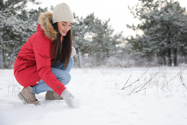 Young woman rolling snowball outdoors on winter day. Space for text - Foto, afbeelding