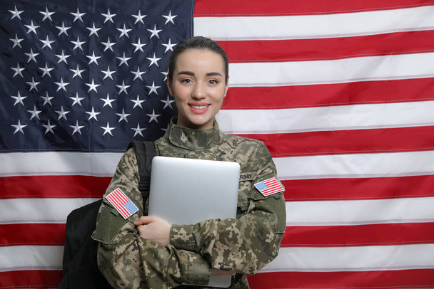 Female soldier with backpack and laptop near flag of United States. Military education - Zdjęcie, obraz