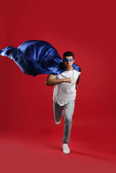 Man in superhero cape and mask running on red background - Foto, afbeelding