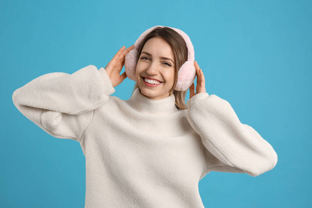 Happy woman wearing warm earmuffs on light blue background - Фото, изображение