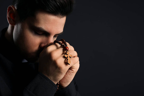 Priest with rosary beads praying on black background, closeup. Space for text - Фото, зображення