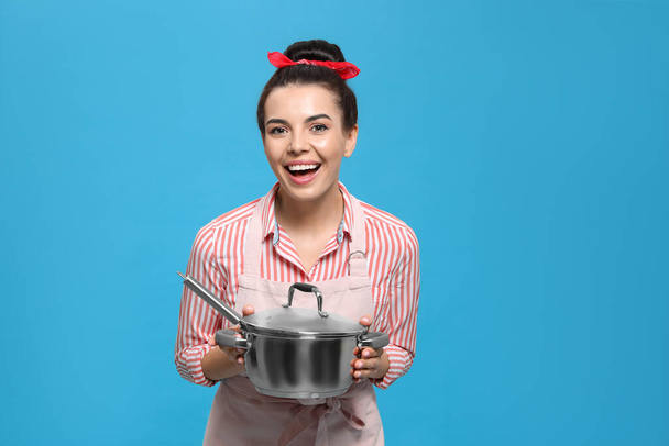 Housewife with pan on light blue background - Фото, изображение
