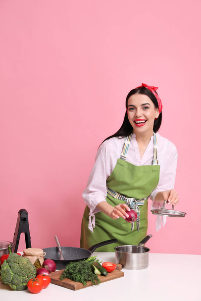 Young housewife cooking at white table on pink background. Space for text - Fotó, kép