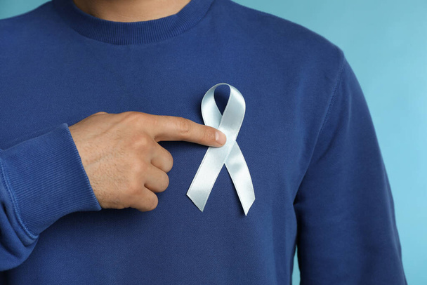 Man with ribbon on light blue background, closeup. Urology cancer awareness - Fotoğraf, Görsel