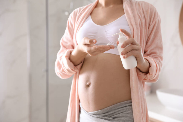 Junge schwangere Frau mit kosmetischem Produkt im Badezimmer, Nahaufnahme. Raum für Text - Foto, Bild