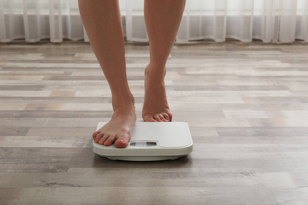 Женщина наступает на весы в помещении, крупным планом. Контроль веса - Фото, изображение