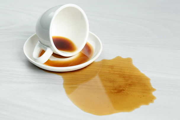 Overturned cup and spilled coffee on white wooden table - Foto, imagen