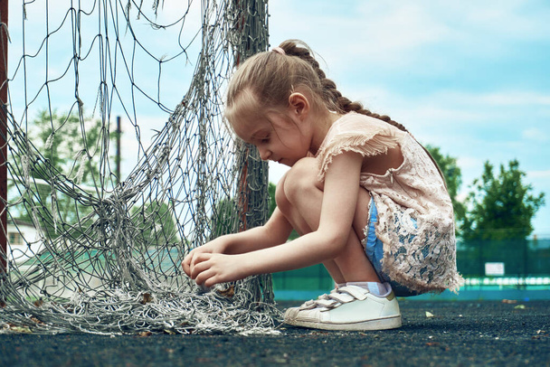 Una niña se pone en cuclillas con un juguete en las manos, una niña juega al aire libre. Tiempo de verano, cielo azul. - Foto, imagen