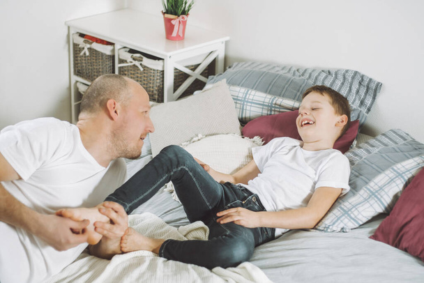 Otec si hraje se svým synem 7-10 v posteli. Táta lechtá děti na nohou. Rodina, bavte se - Fotografie, Obrázek