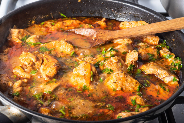 Kotitekoinen kana curry keitetään paistinpannulla. Kananpalat keitetään punaisessa kastikkeessa voin ja hienonnettu korianteri, lähikuva - Valokuva, kuva
