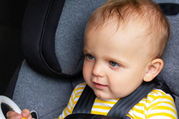 Happy caucasian baby boy in yellow striped t-shirt sitting in grey car seat and holding toy in hand. Child transportation safety.  - Foto, immagini