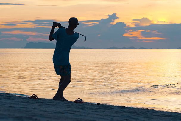 Silhouette of a adult man playing golf on the beach against the backdrop of a beautiful sunset - Foto, Imagen