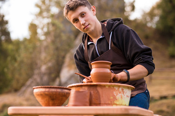 Muž hrnčíř pracovat s hliněným nádobím. Mladý muž hrnčíř na jeho dílně s přírodním zázemím - Fotografie, Obrázek