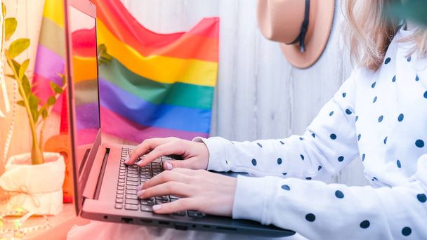 Young millennial hippie woman sitting on balcony using laptop. LGBTQ rainbow flag on background. Online education tuition. Work from home. Modern office. - Foto, afbeelding