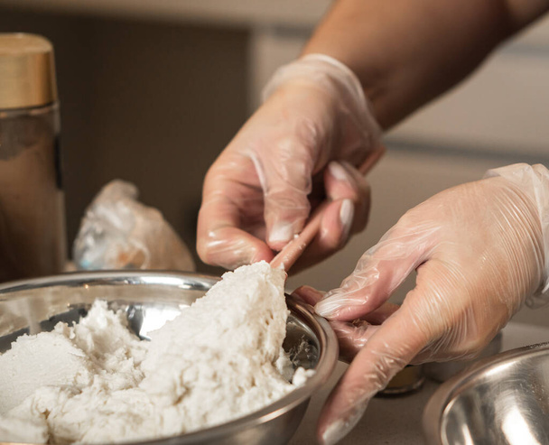 Hands with transparent gloves handling butter cream in a metal bowl. - Foto, Bild