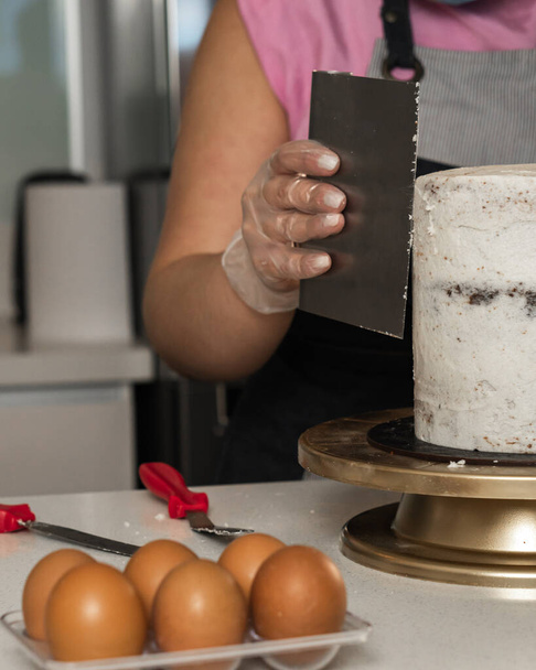 Νεαρή γυναίκα διακόσμηση κέικ με αυγά και συστατικά στο τραπέζι - Φωτογραφία, εικόνα