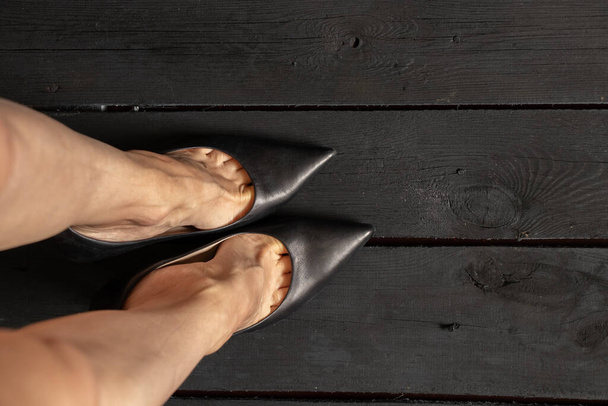женские ноги в черных туфлях на высоких каблуках на черном деревянном полу, вид снизу, женская обувь - Фото, изображение