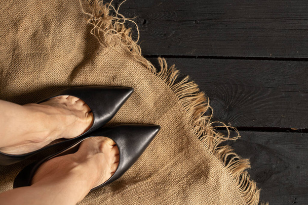 vrouwelijke benen in zwarte schoenen met hoge hakken op een zwarte houten vloer en bruine stof, onderaanzicht, damesschoenen - Foto, afbeelding