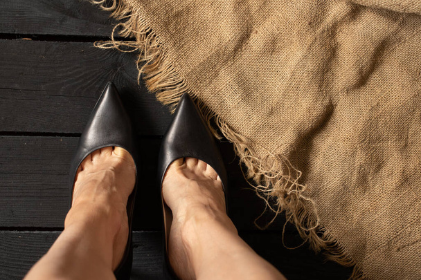 kobiece nogi w czarnych butach na wysokim obcasie na czarnej drewnianej podłodze i brązowej tkaninie, widok na dno, damskie buty - Zdjęcie, obraz