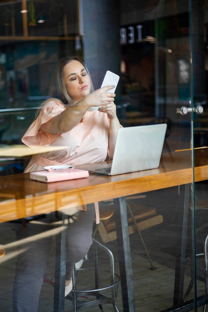Beautiful plus size business woman posing taking selfie use smartphone working remotely at cafe - Valokuva, kuva