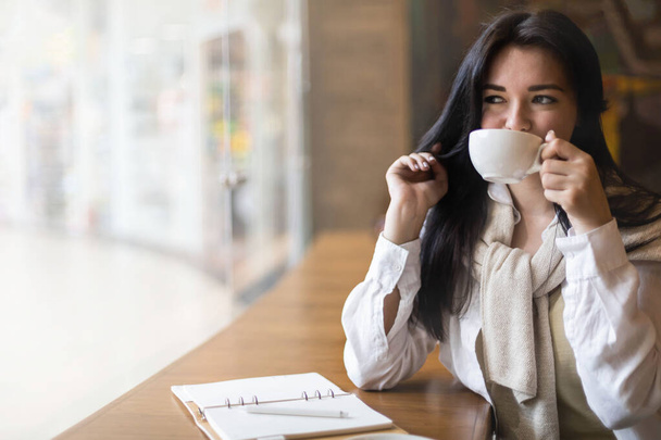 Beautiful mixed race female smiling dreaming writing diary sitting at cafeteria with coffee cup - Foto, imagen