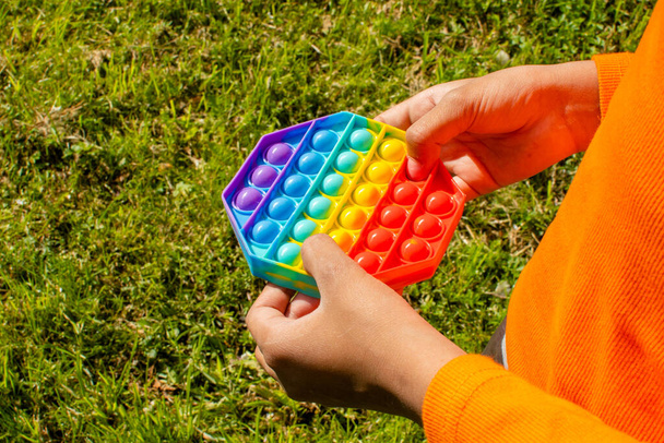 Colorful antistress sensory toy fidget push pop it in kid's hands. Pop it toy. Girl plays outside. Outdoor - 写真・画像