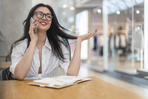 Cheerful business woman talking smartphone smiling having positive emotion at modern shopping mall - Fotó, kép