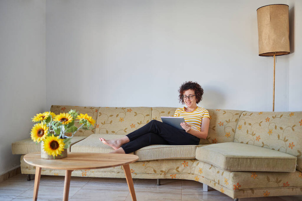 Женщина сидит на диване с помощью цифрового планшета - Фото, изображение