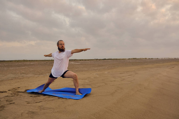 Man practices warrior two pose at sea beach - Foto, Imagem