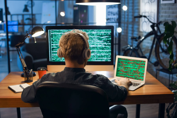 Junger Programmierer arbeitet nachts mit Computer und Laptop im Büro - Foto, Bild